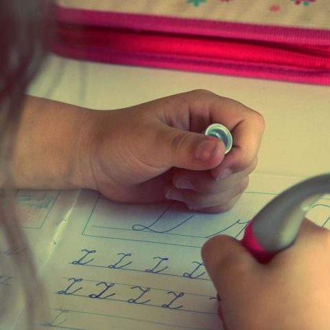 La main d’un enfant qui trace des lettres en attaché sur son cahier de classe.