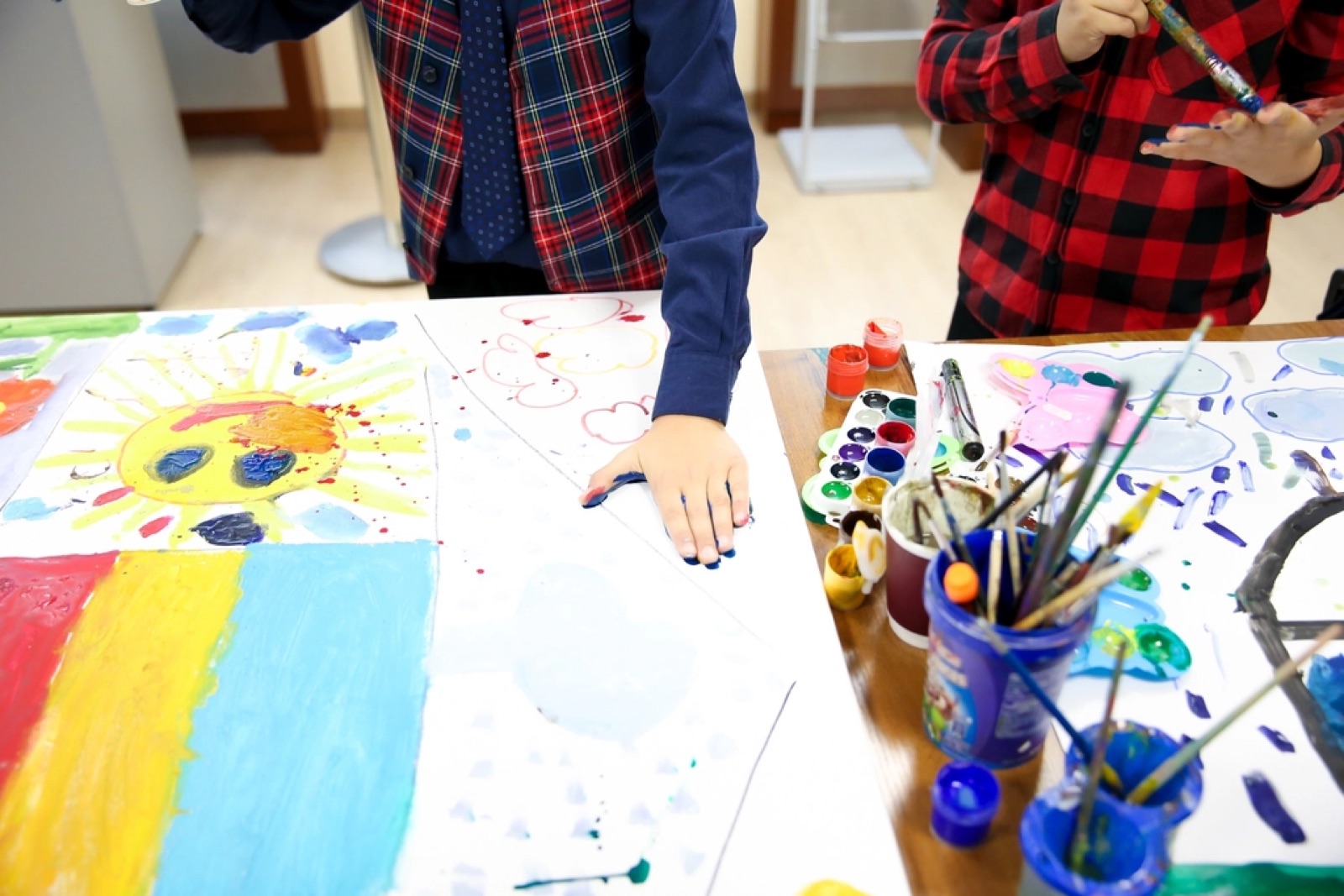 Des enfants peignent autour d'une table couverte de gouaches et de pinceaux